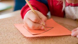 a child hand holds a pencil and traces a triangle on orange paper