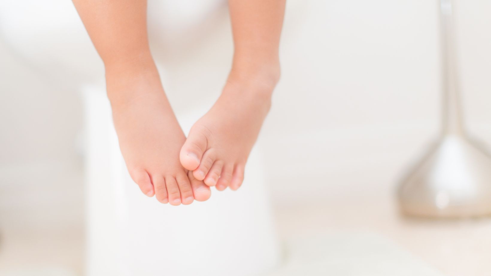 a child's feet dangle from a white toilet