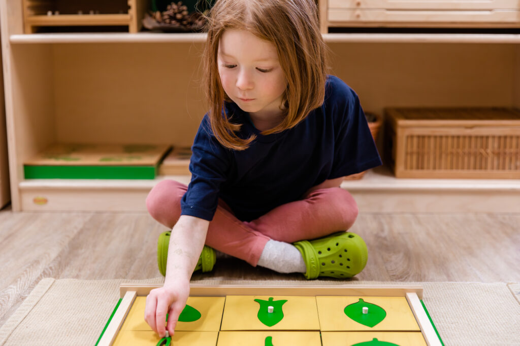 A young girl with red hair and a blue shirt places pieces in a yellow and green puzzle. 