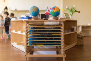 two globes placed on top of a wooden cabinet that has narrow shelves holding puzzle maps