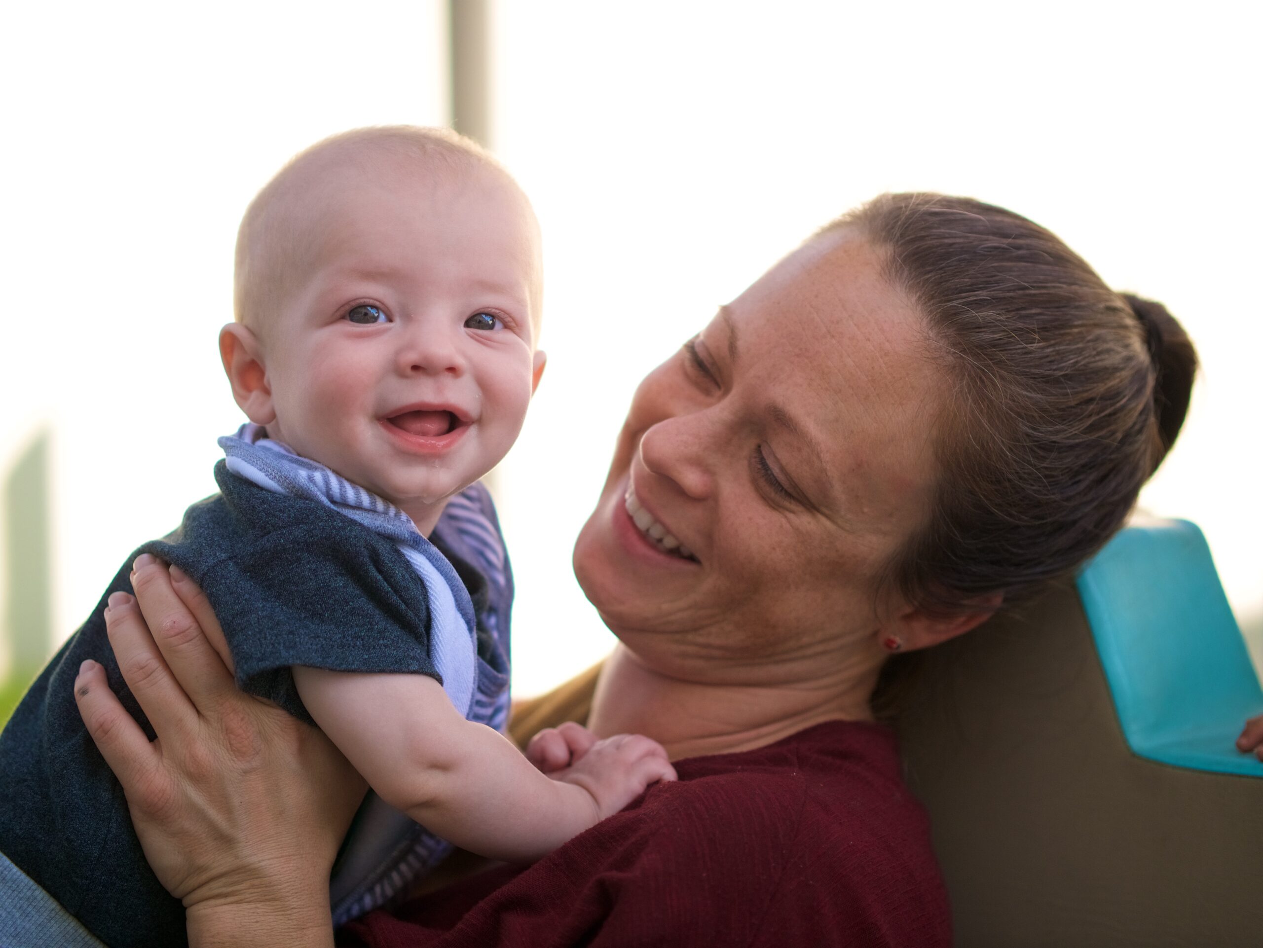 A teacher with long hair and a maroon shirt holds a baby with a blue shirt