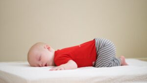 A baby in black and white striped pants and a red t-shirt leads on his stomach